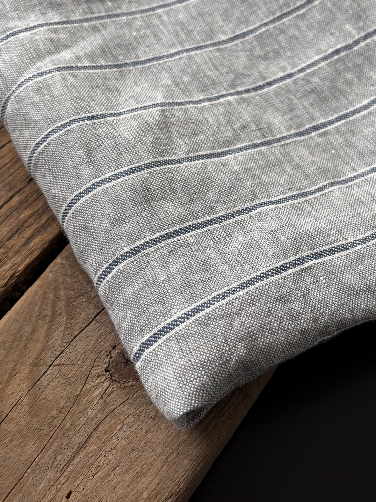 Stripet kjøkkenhåndkle i 100 % lin med blå detaljer på trebord.